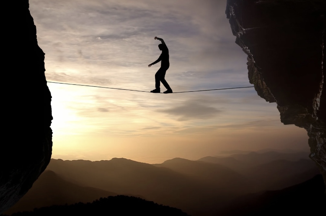 Mann balanciert auf einem Seil zwischen zwei Felsen, symbolisiert die Risiken und Vorsichtsmaßnahmen der Kardioversion